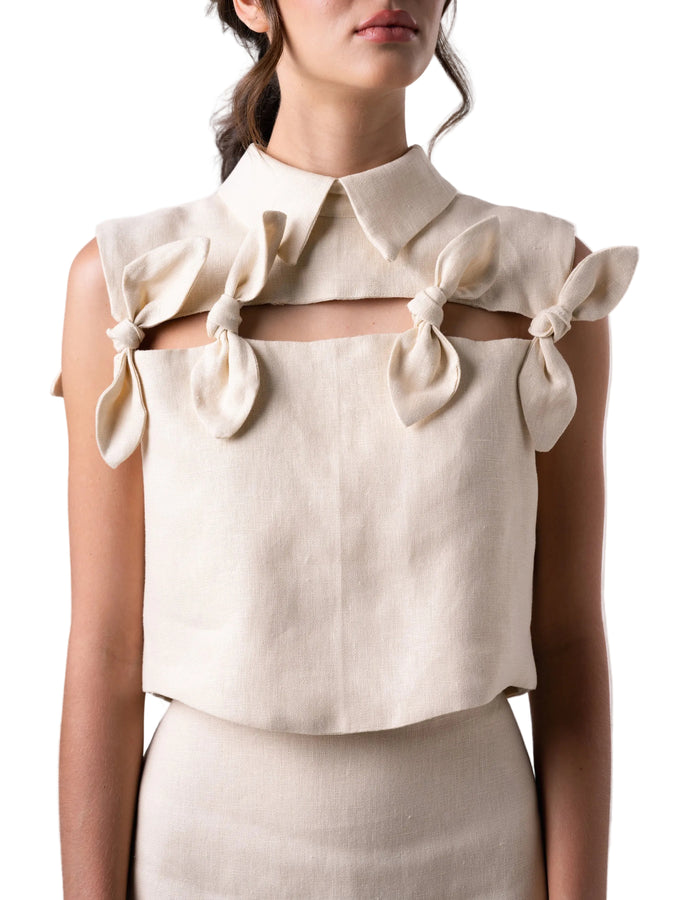 Top with a cropped boxy silhouette, classic collar, cut out detail accentuated with petal knot details, and back button down closure.