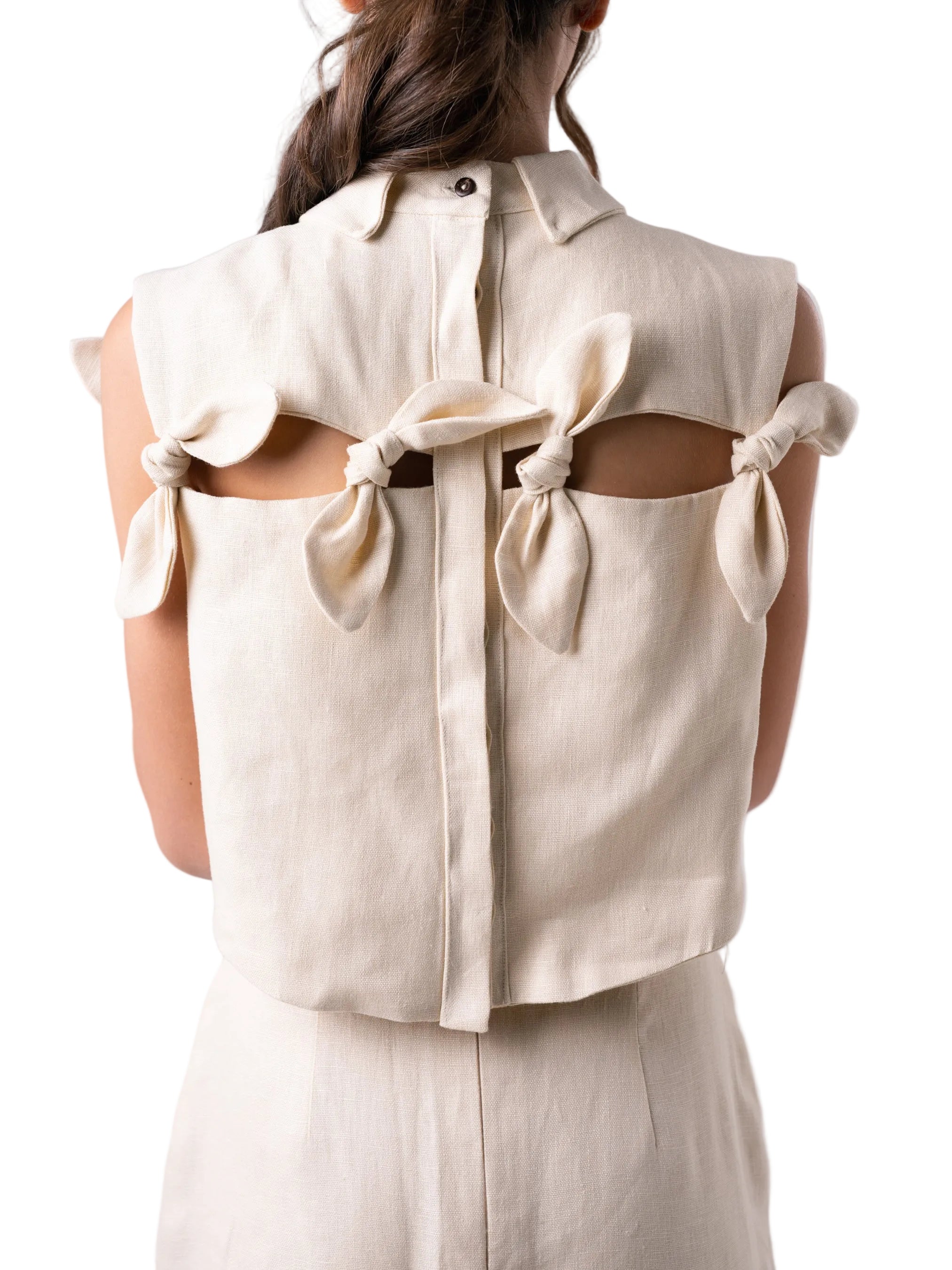 Top with a cropped boxy silhouette, classic collar, cut out detail accentuated with petal knot details, and back button down closure.