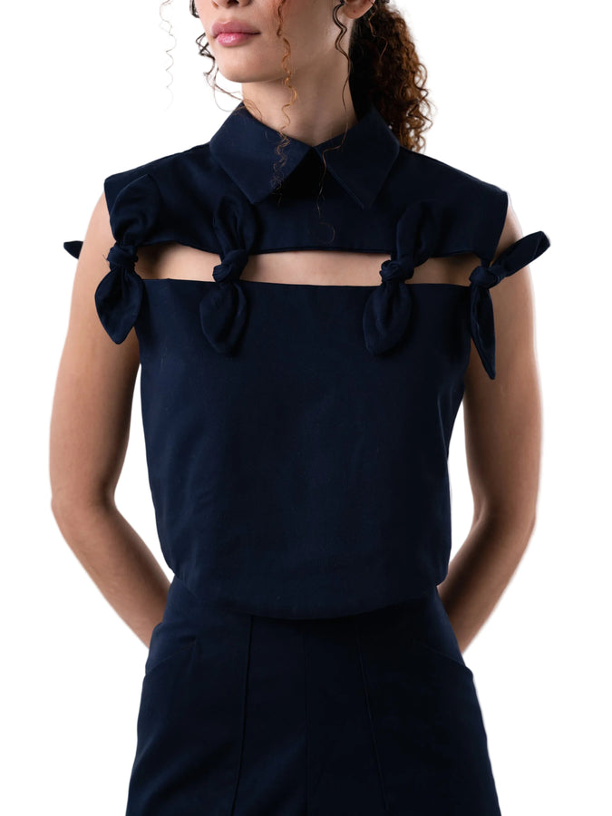 Cropped top boxy silhouette, with classic collar, cut out detail accentuated with petal knot details, and back button down closure.