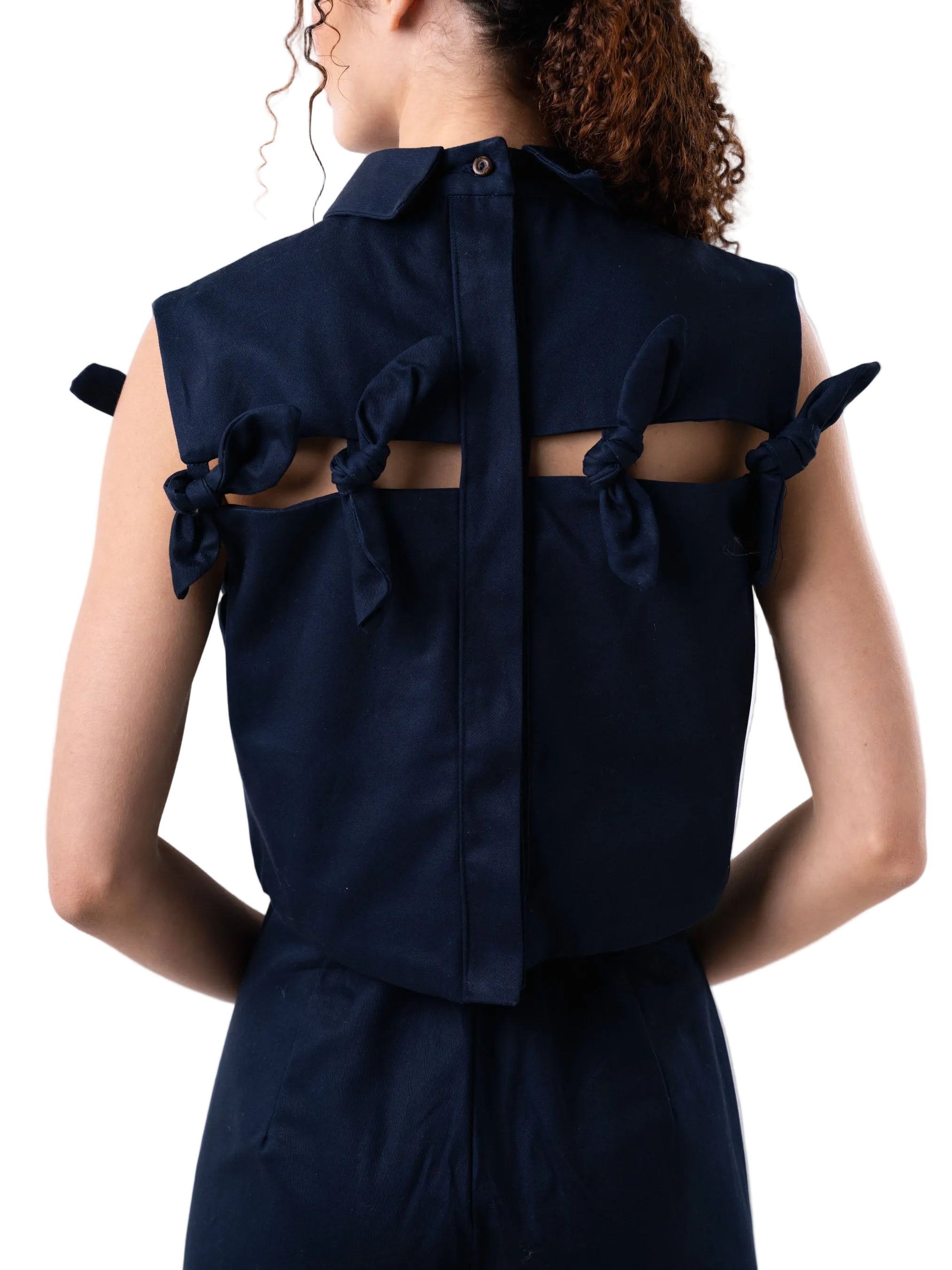 Cropped top boxy silhouette, with classic collar, cut out detail accentuated with petal knot details, and back button down closure.