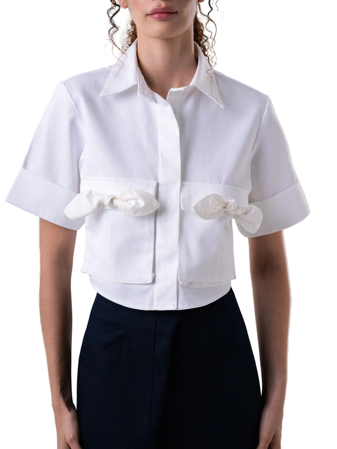 Top that features cropped short sleeve silhouette, classic open collar, sleeve cuff, front button down closure and cargo pockets with petal knot detail.